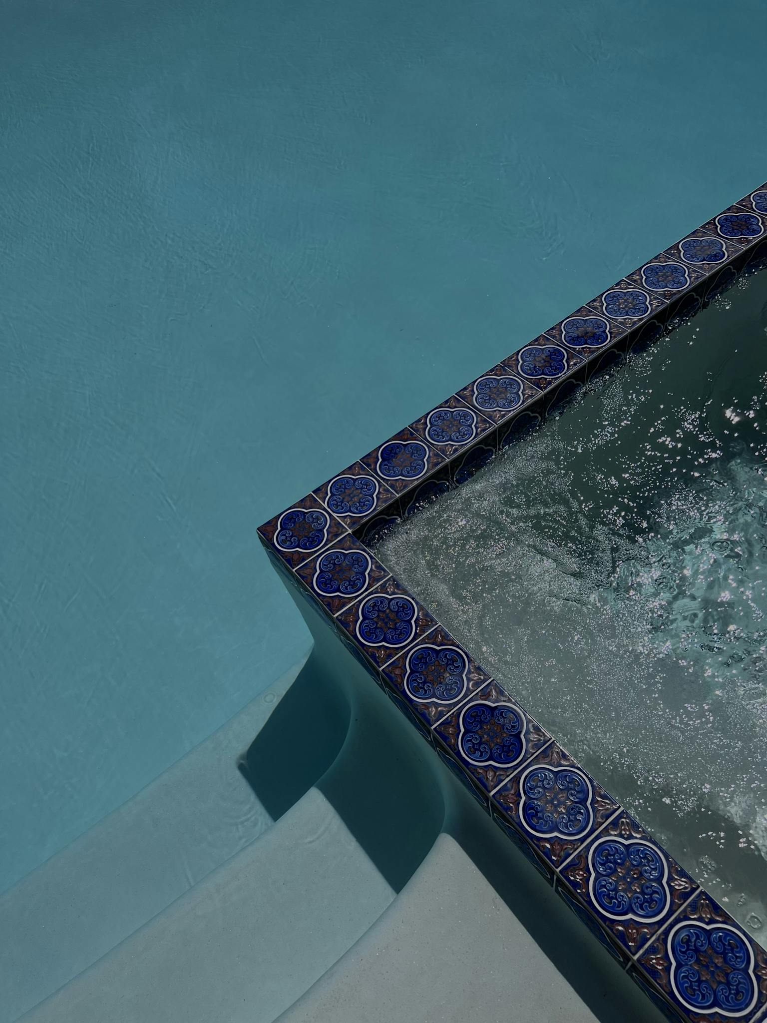 High angle view of a swimming pool with intricate blue tiles and water ripples.